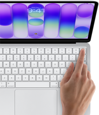 MacBook Neo, Farbe Silber, Anmeldebildschirm, ein Finger berührt den Touch ID Sensor oben rechts auf der Tastatur
